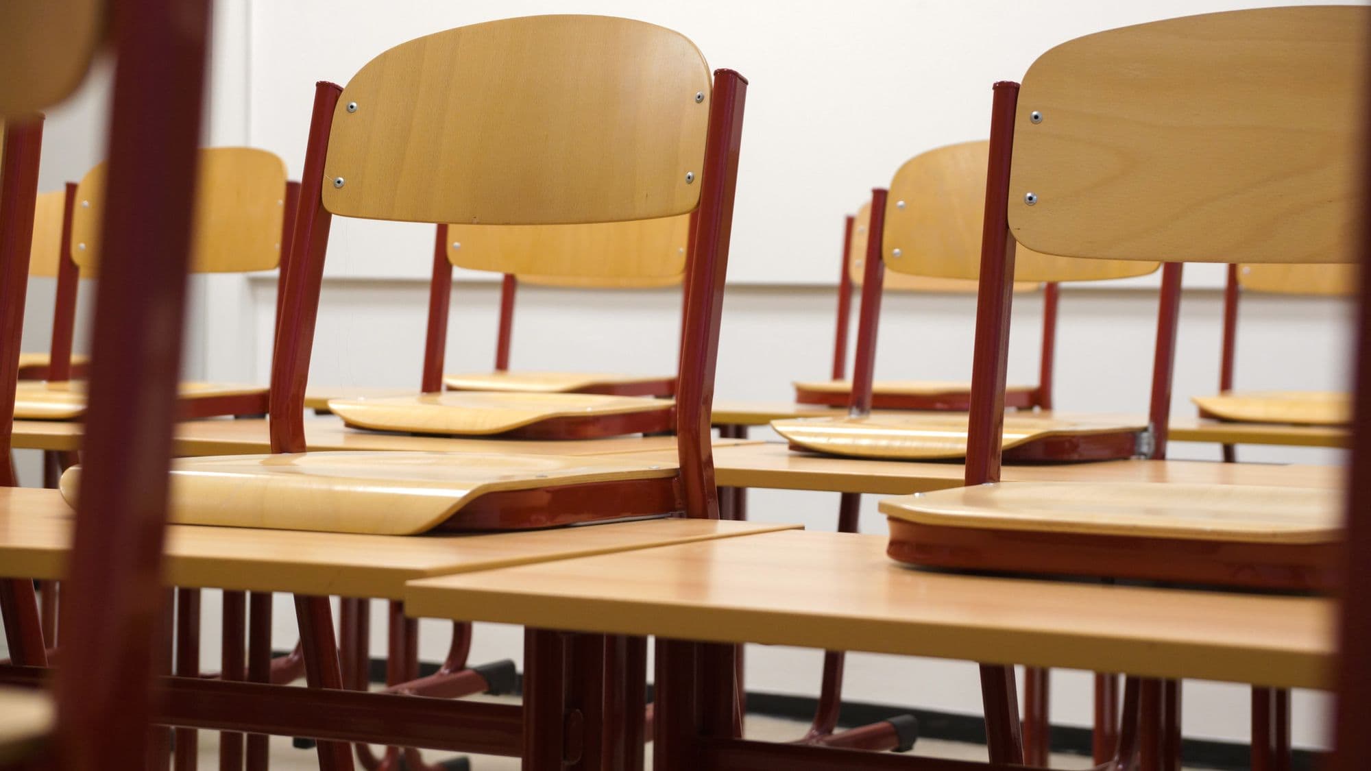 Sala de aula ampla com mesas e cadeiras de madeira organizadas para os alunos